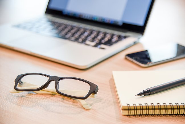 Glasses,-binder-notebook,-pen-and-laptop-on-wooden-office-desk-